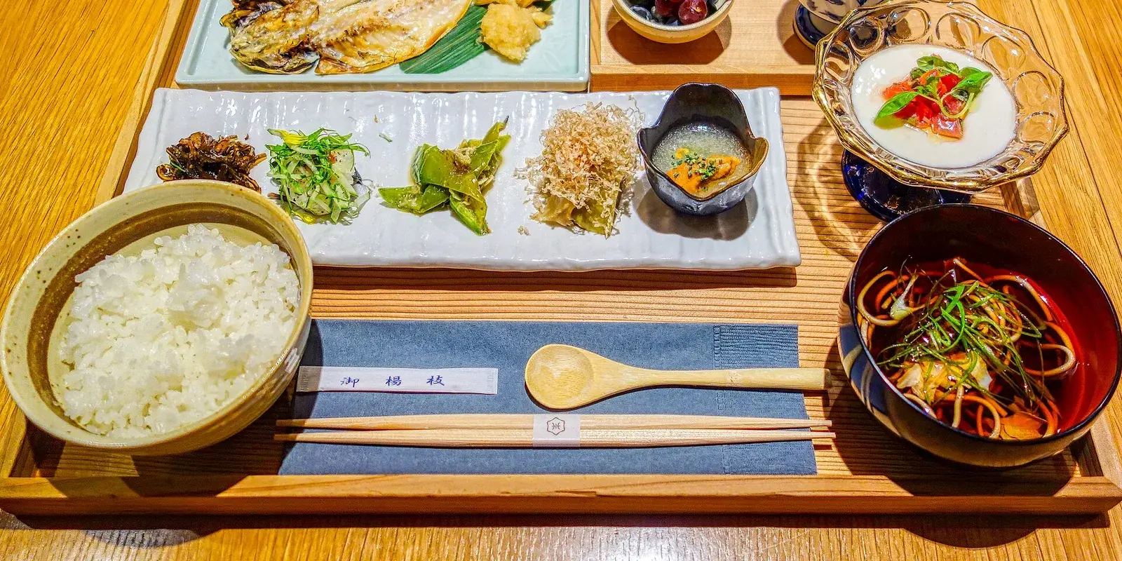 Traditional Japanese breakfast set on a wooden tray with grilled fish, rice, miso, small side dishes, and chopsticks resting on a holder
