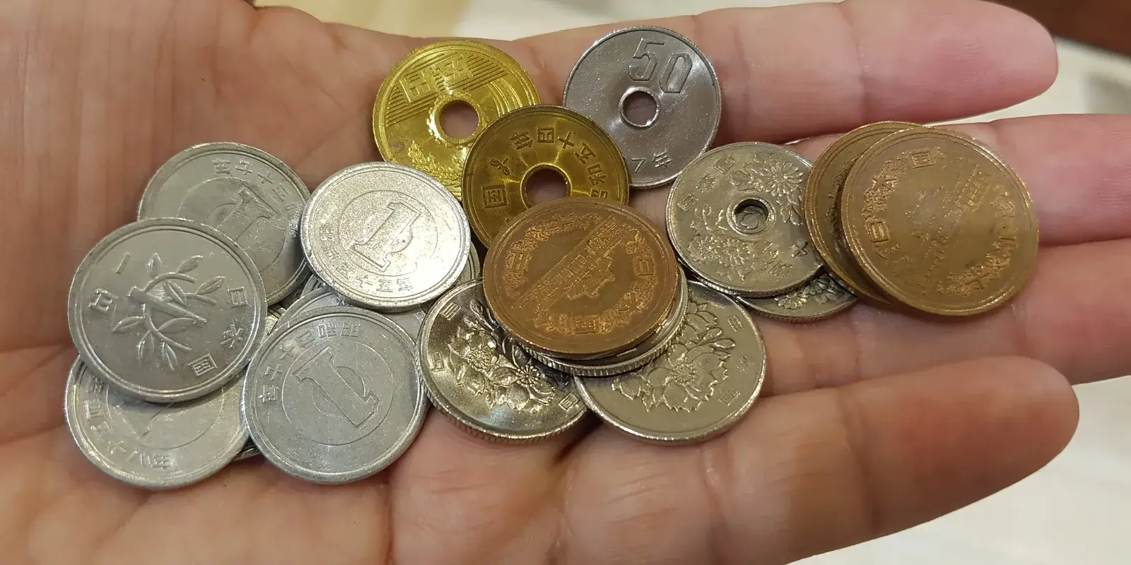 An open palm holding an assortment of Japanese yen coins, including 1, 5, 10, and 50 yen pieces
