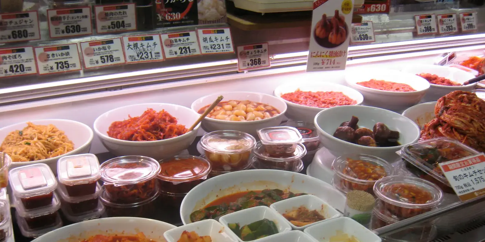 Depachika deli counter in a Japanese department store food hall, with prepared side dishes in white bowls and clear containers under illuminated yen price tags