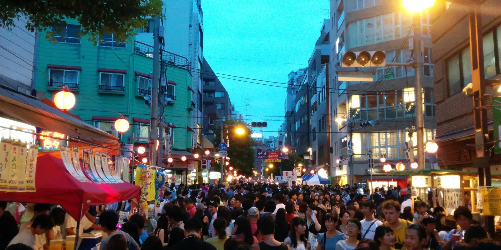 Crowd strolling a lantern-lit summer festival street with food stalls at twilight in Azabu-Juban, Tokyo
