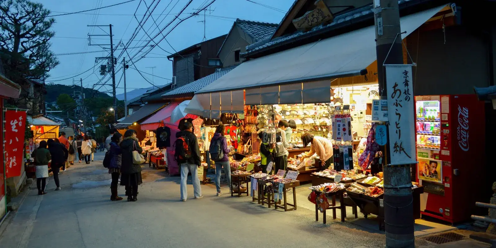 Warm evening view of a traditional Kyoto souvenir shop street with visitors browsing lantern-lit stalls