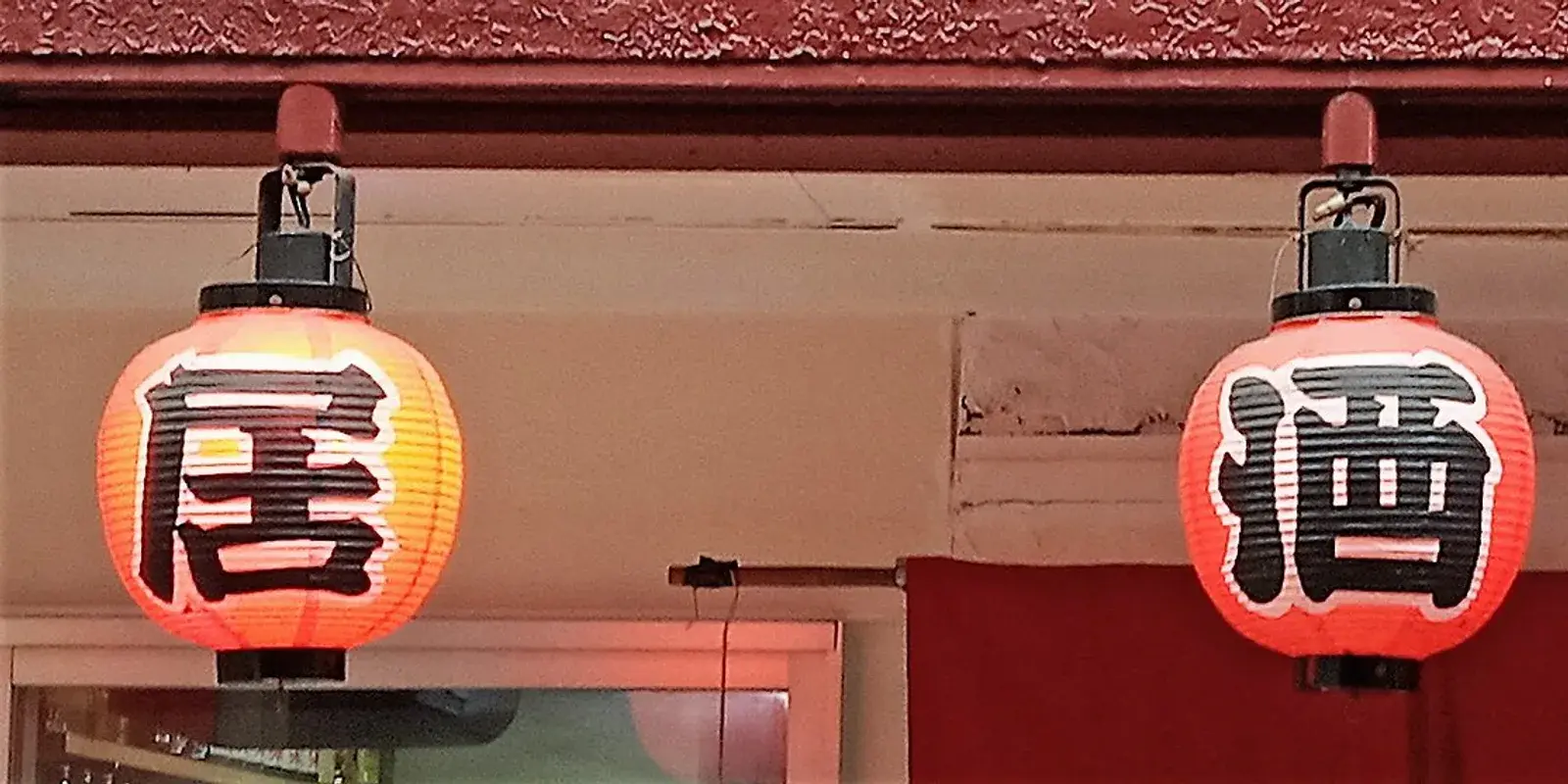 Three red paper lanterns reading izakaya hang outside a Japanese pub at dusk