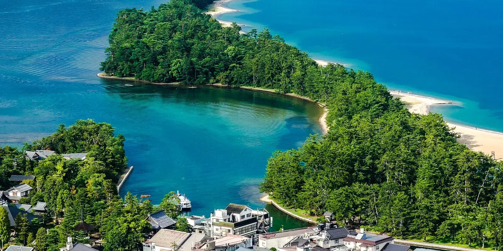 Aerial view of the pine-covered Amanohashidate sandbar curving across the turquoise waters of Miyazu Bay