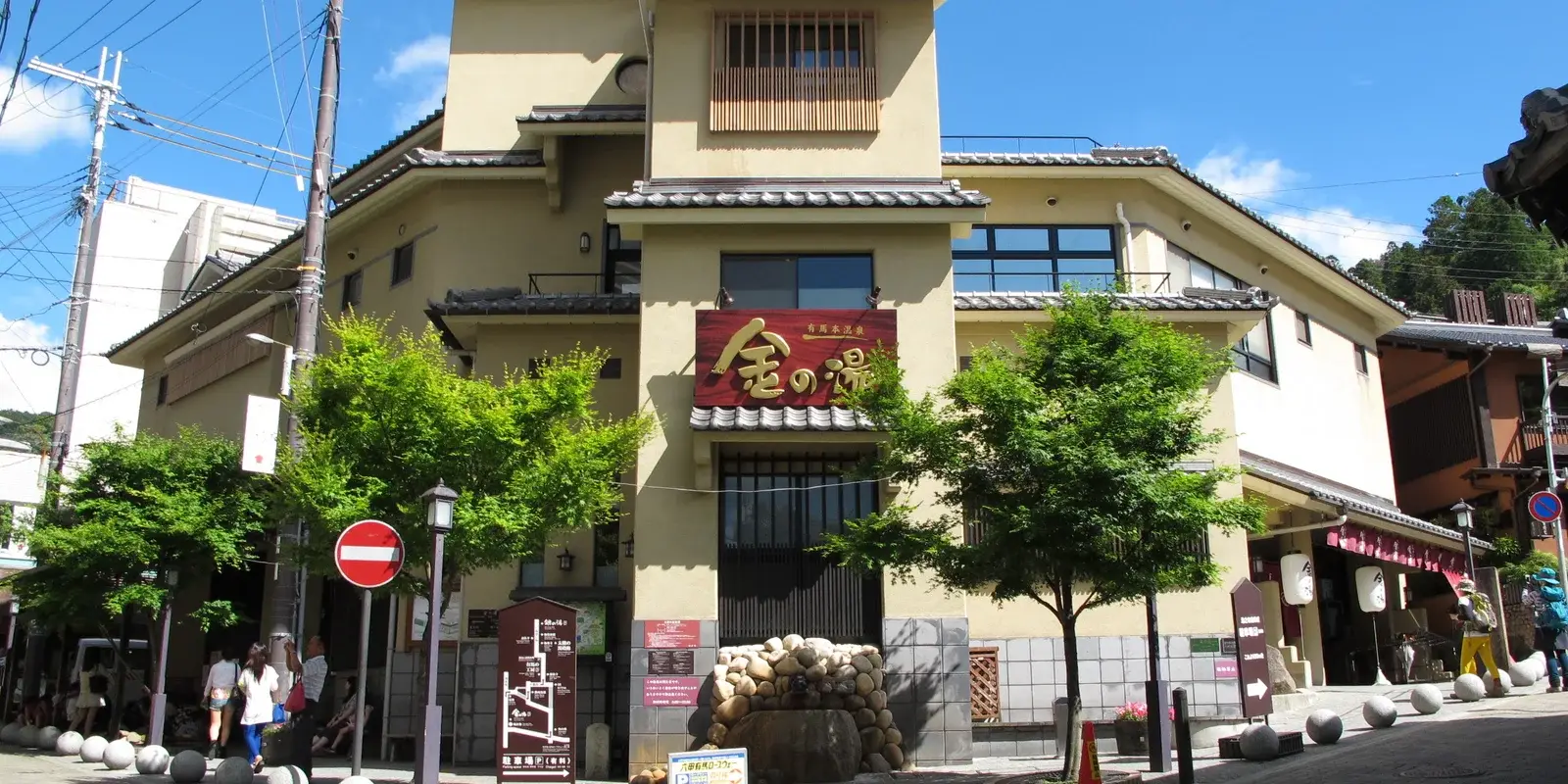 The Kin-no-yu public bathhouse in Arima Onsen on a sunny day, with its red sign and gold lettering above the entrance