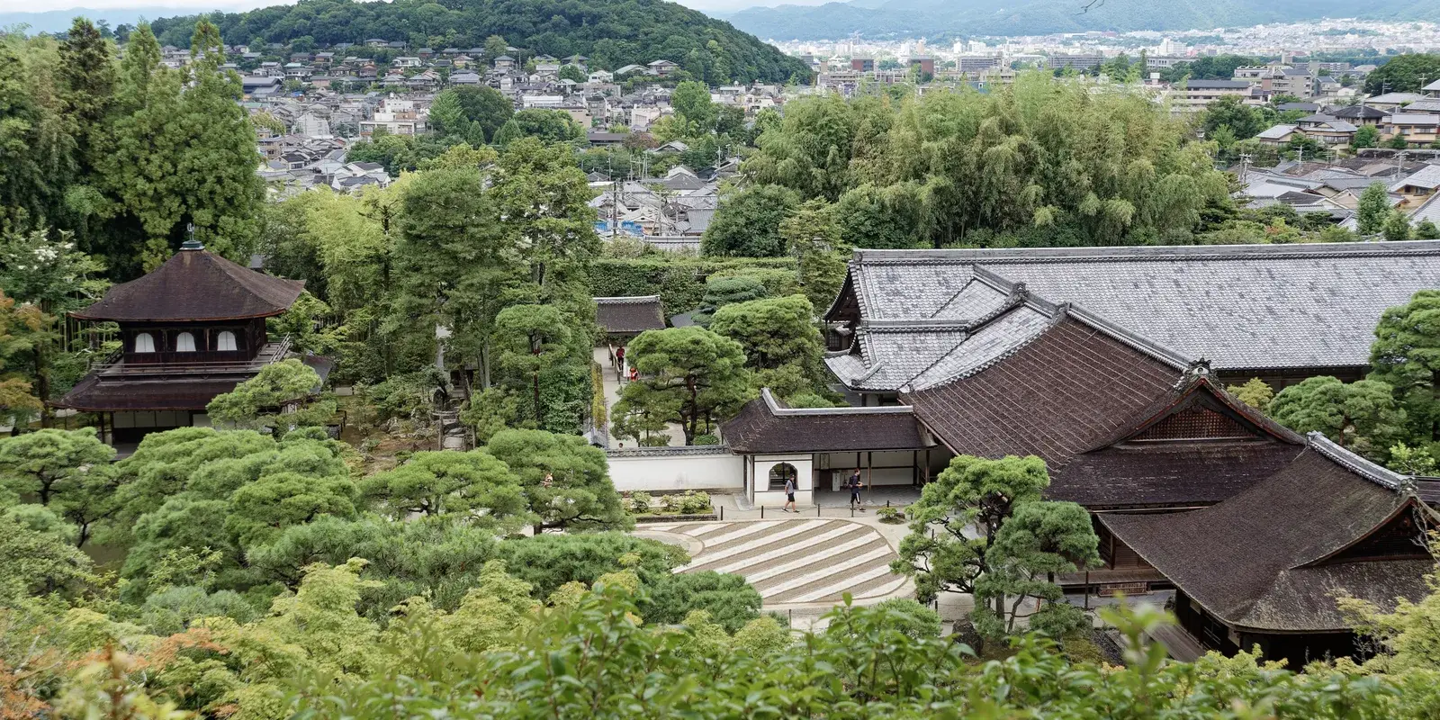 Ginkaku-ji from the hillside viewpoint: the dark wooden Silver Pavilion, the raked sea of silver sand, the temple roofs, and north Kyoto beyond