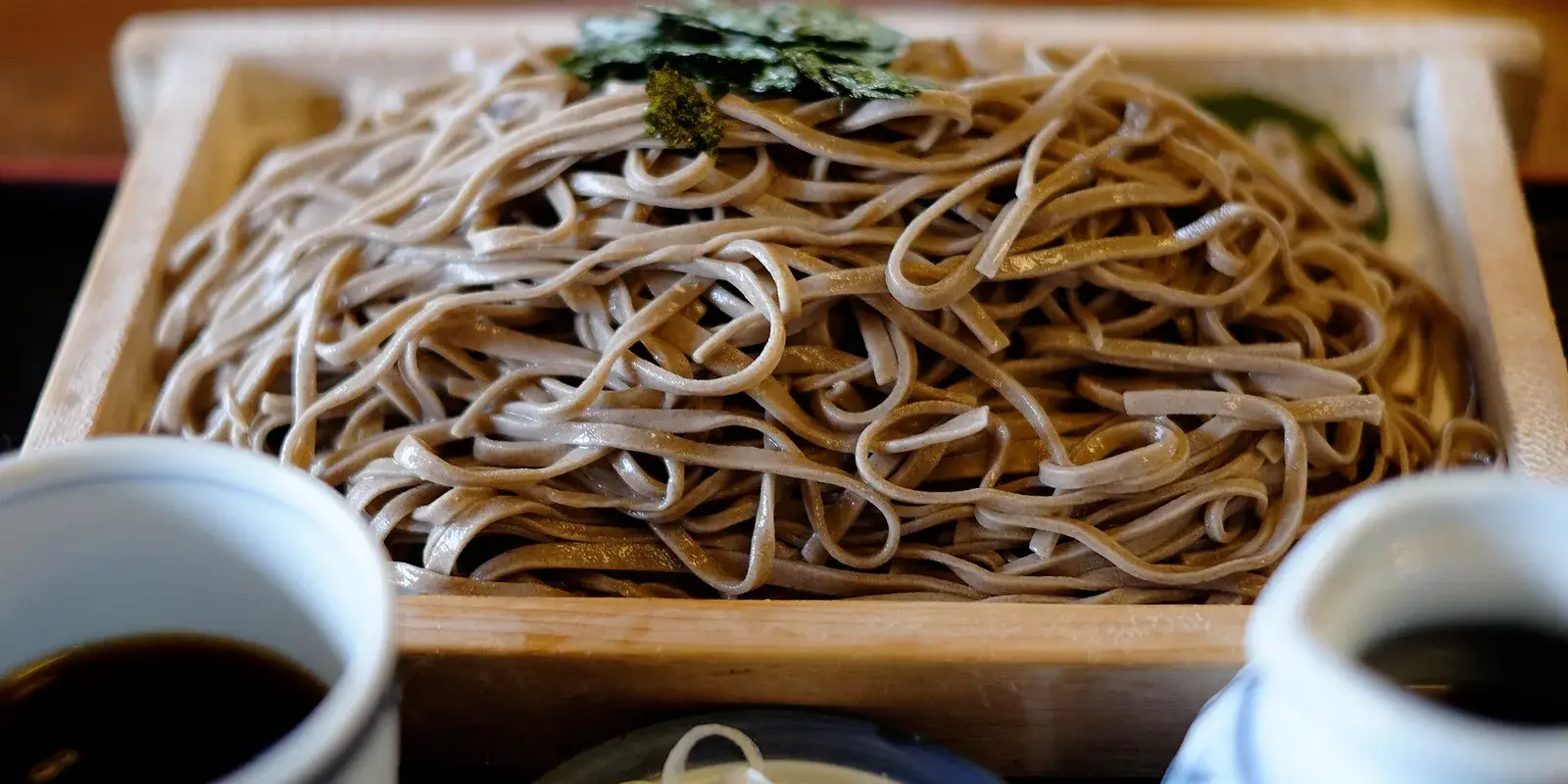 A bamboo tray of cold mori soba buckwheat noodles topped with shredded nori, served with dipping sauce cups and condiments in a Japanese restaurant