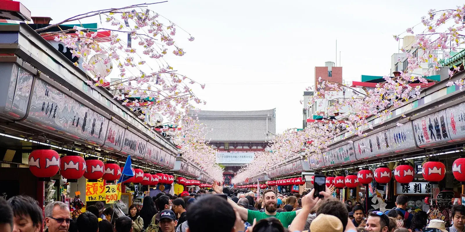 Dense crowd of visitors fills Nakamise-dori shopping street leading to Senso-ji Temple's Hozomon gate in Asakusa, Tokyo, with rows of red lanterns overhead