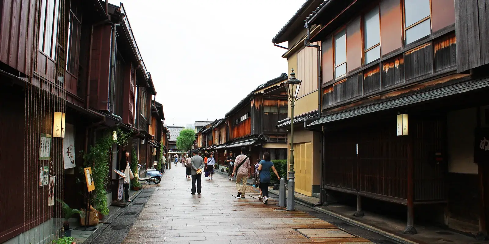 The wooden-latticed teahouse street of the Higashi Chaya district in Kanazawa, with a gas lamp and a few distant strollers on the paving