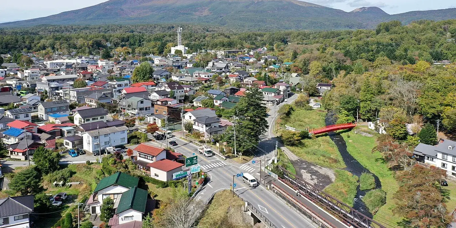 Aerial view of Naka-Karuizawa town with Mount Asama rising behind the rooftops and a red bridge over the Yukawa river