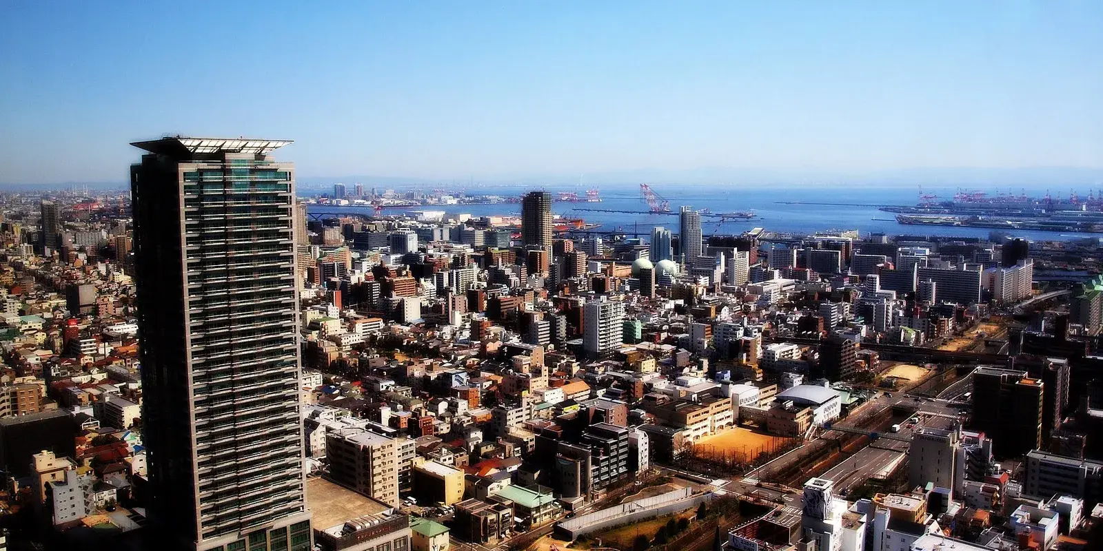 Kobe by day seen from above, the dense city packed onto the narrow strip of land between the green mountains and Osaka Bay