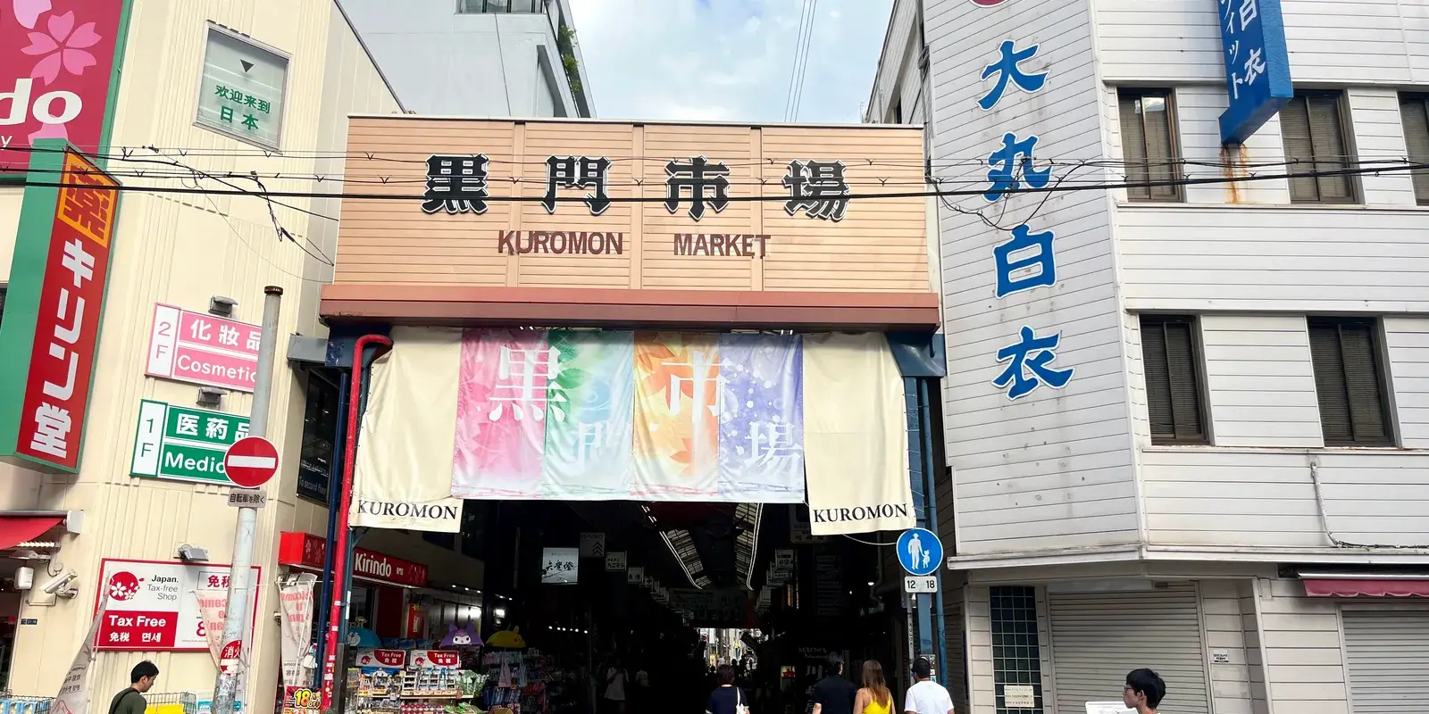 The wooden entrance sign of Kuromon Market in Osaka, reading Kuromon Market in Japanese and English above the covered arcade entrance