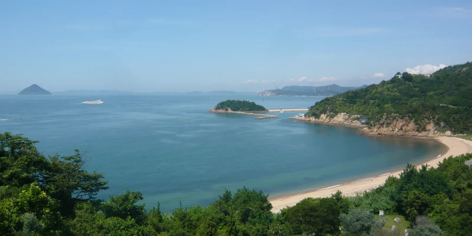 The calm Seto Inland Sea seen west from Naoshima — a ferry crossing toward a green island and a curving beach, with distant mainland smelter stacks on the horizon