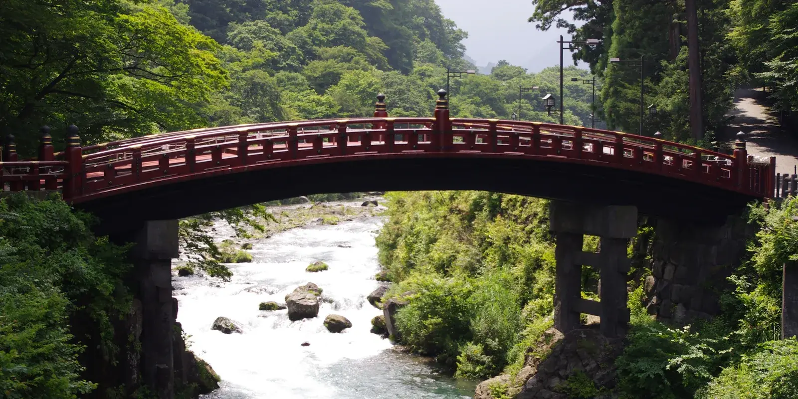 The vermilion Shinkyo bridge arching over the green Daiya River at the forested entrance to Nikko