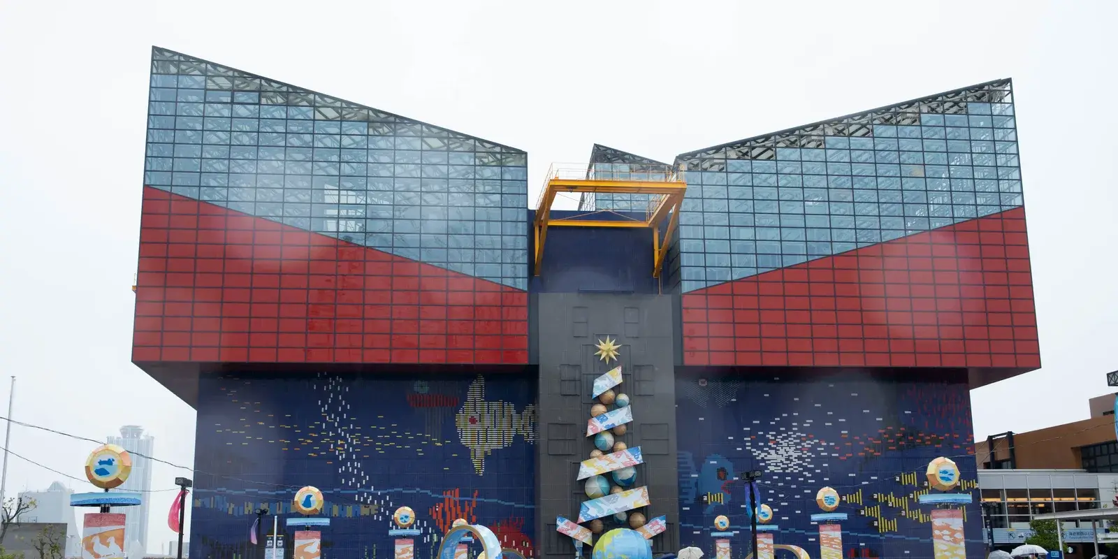 The blue and red banded exterior of Osaka Aquarium Kaiyukan, with a tiled mural of fish and a globe motif across the lower wall