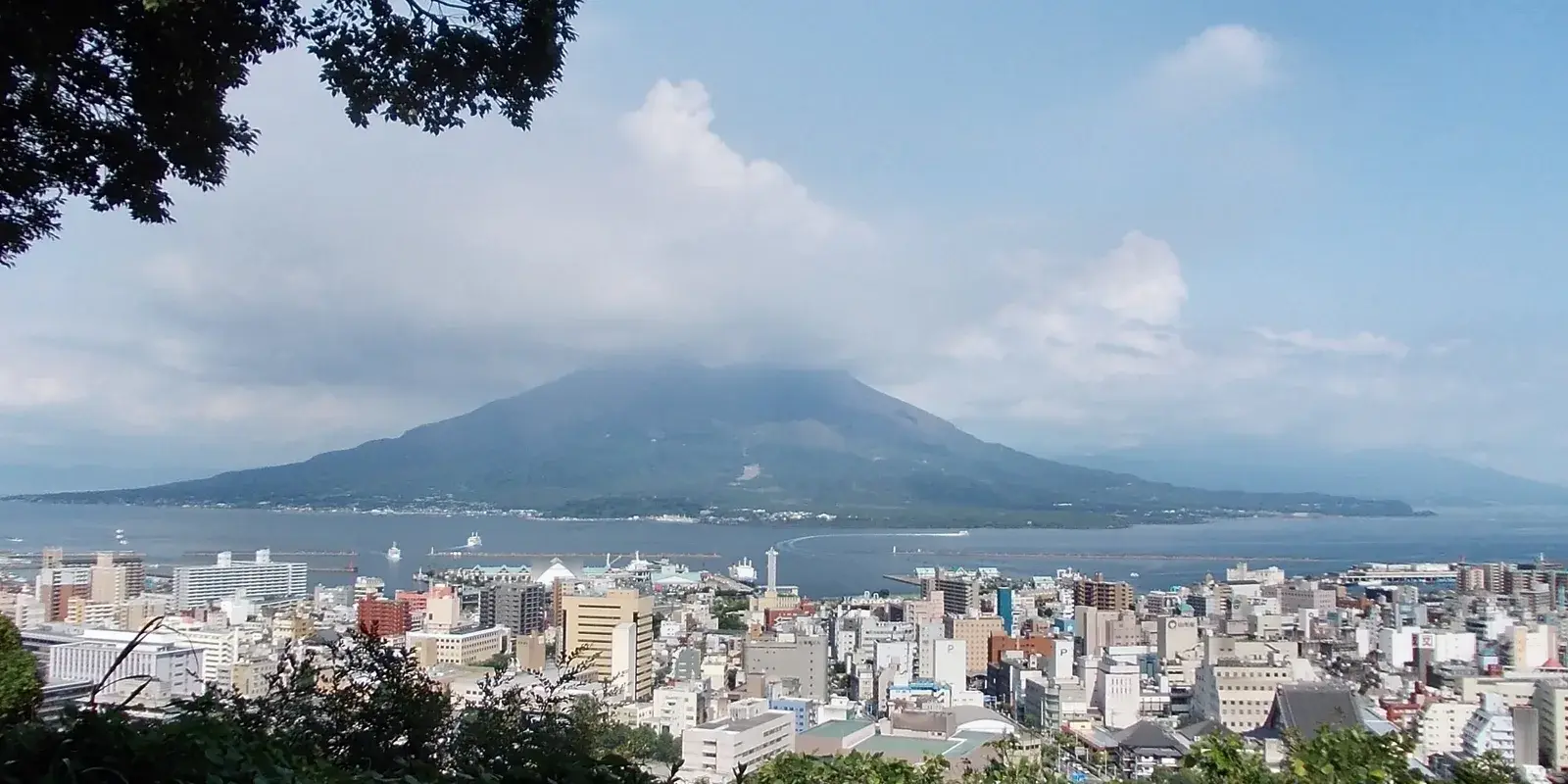 Sakurajima volcano across Kinko Bay, seen over the Kagoshima cityscape from Shiroyama, with cloud clinging to its summit