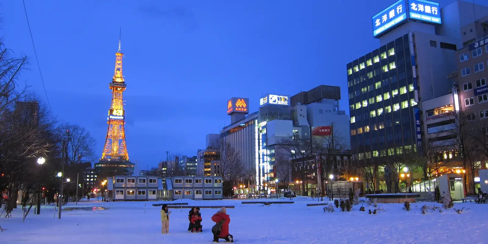 The illuminated Sapporo TV Tower rising over a snow-covered Odori Park at dusk in winter
