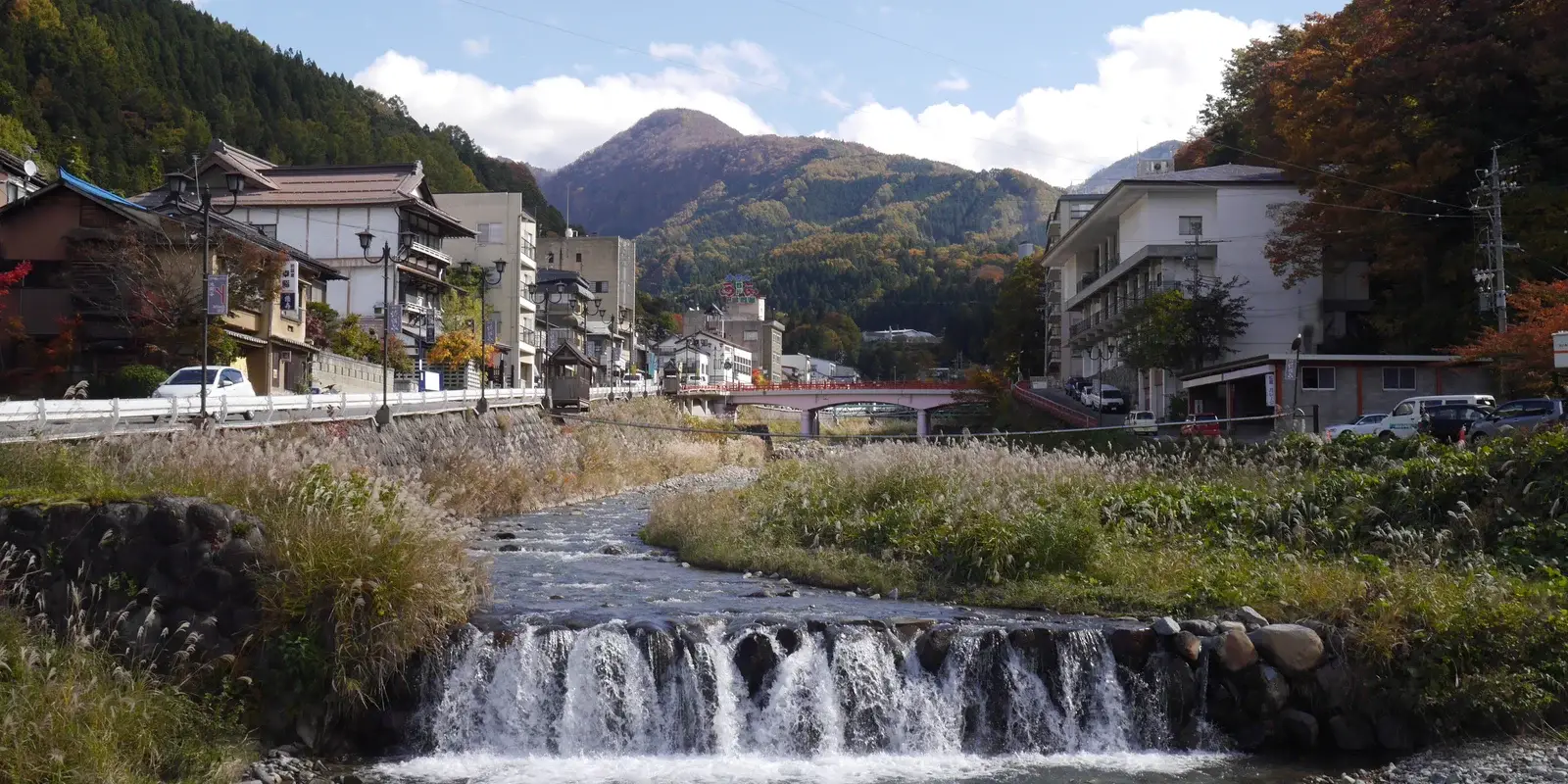 The Yokoyu River running through Shibu Onsen on a clear autumn day, with ryokan buildings along the bank and forested mountains behind