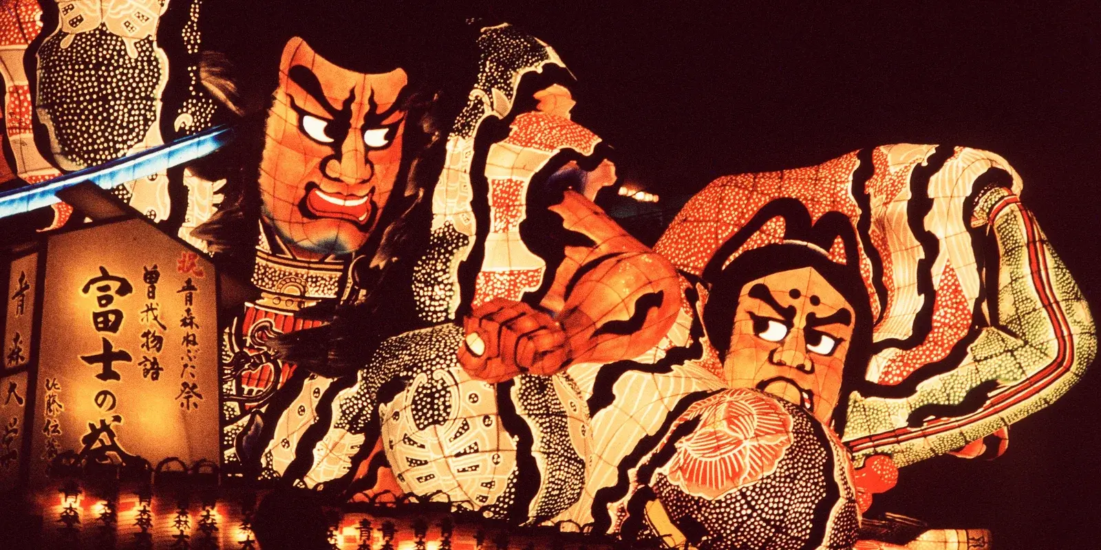Two illuminated Aomori Nebuta warrior floats glowing against the night sky during the parade