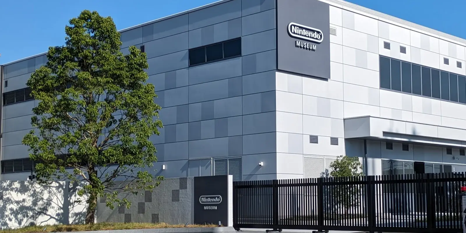 The grey and white exterior of the Nintendo Museum in Uji, Kyoto, with its sign and a gated security fence at the entrance