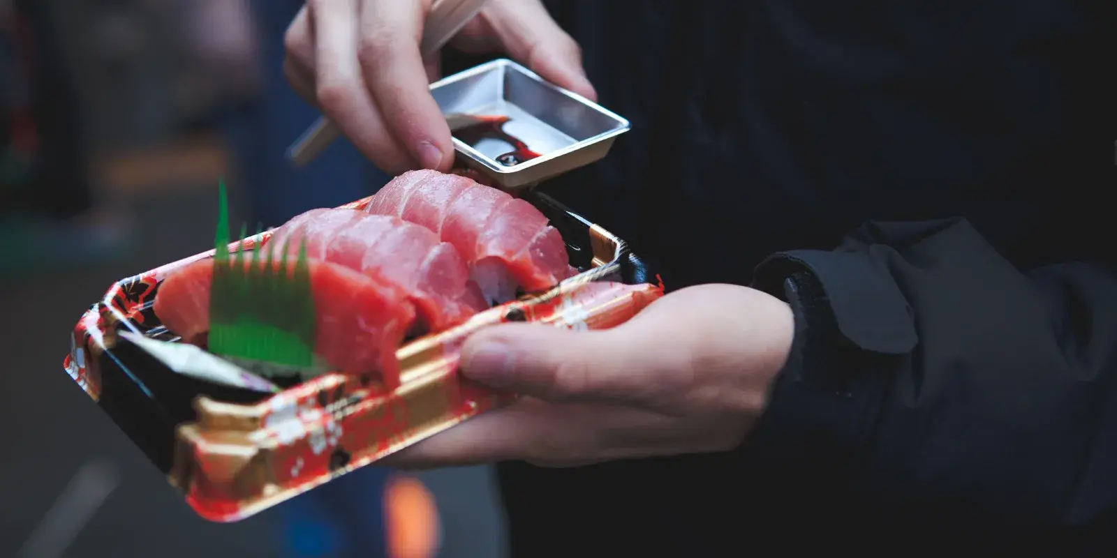 A tray of fresh tuna sashimi held in two hands at a Tokyo fish market, with a small dish of soy sauce