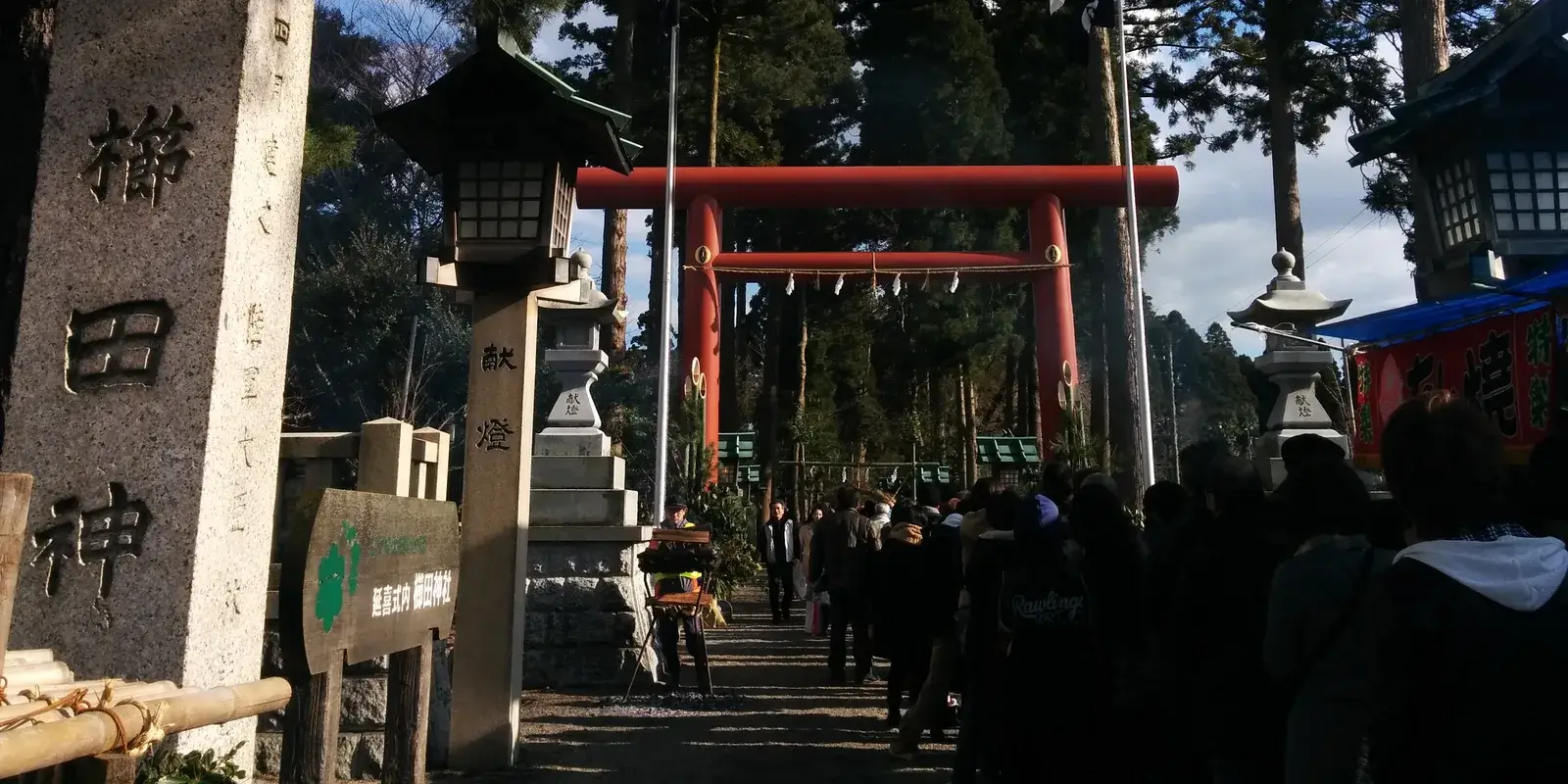 Visitors queueing along a shrine approach beneath a red torii gate and stone lanterns on New Year's Day in Imizu, Toyama