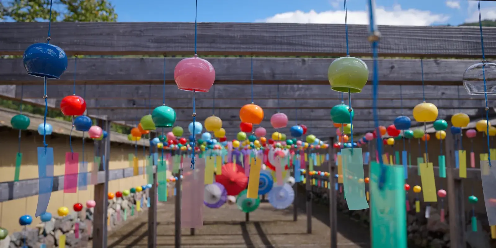 A tunnel of colorful glass furin wind chimes with pastel tanzaku paper strips hanging over a path at a Japanese summer wind chime festival