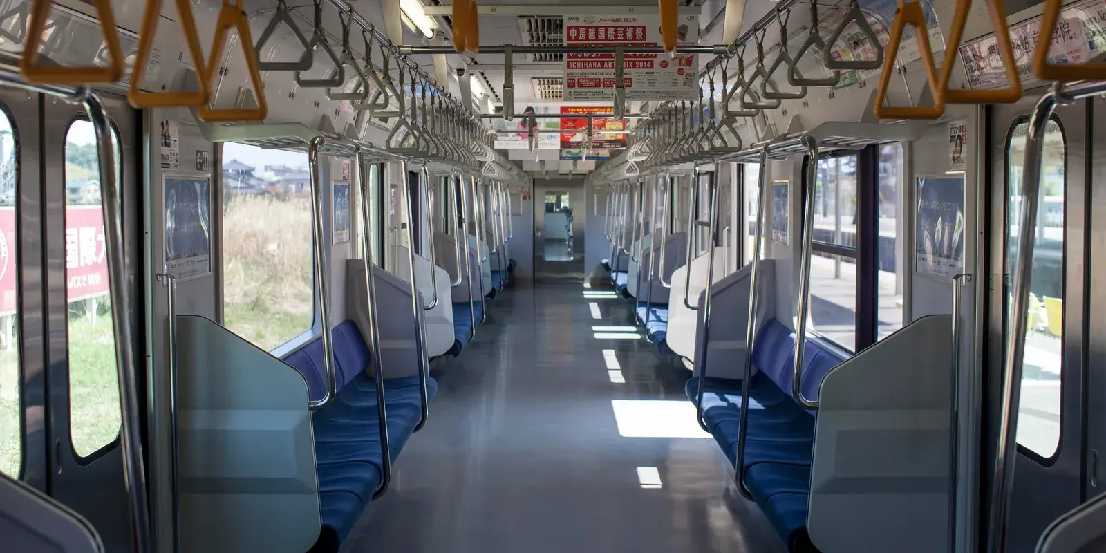 The quiet, sunlit interior of an empty Japanese commuter train, seats and hanging straps in neat symmetry