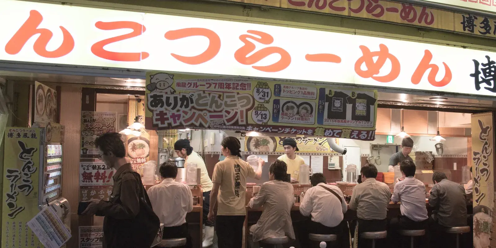 Staff serving customers along the counter of a busy tonkotsu ramen shop in Akihabara, Tokyo