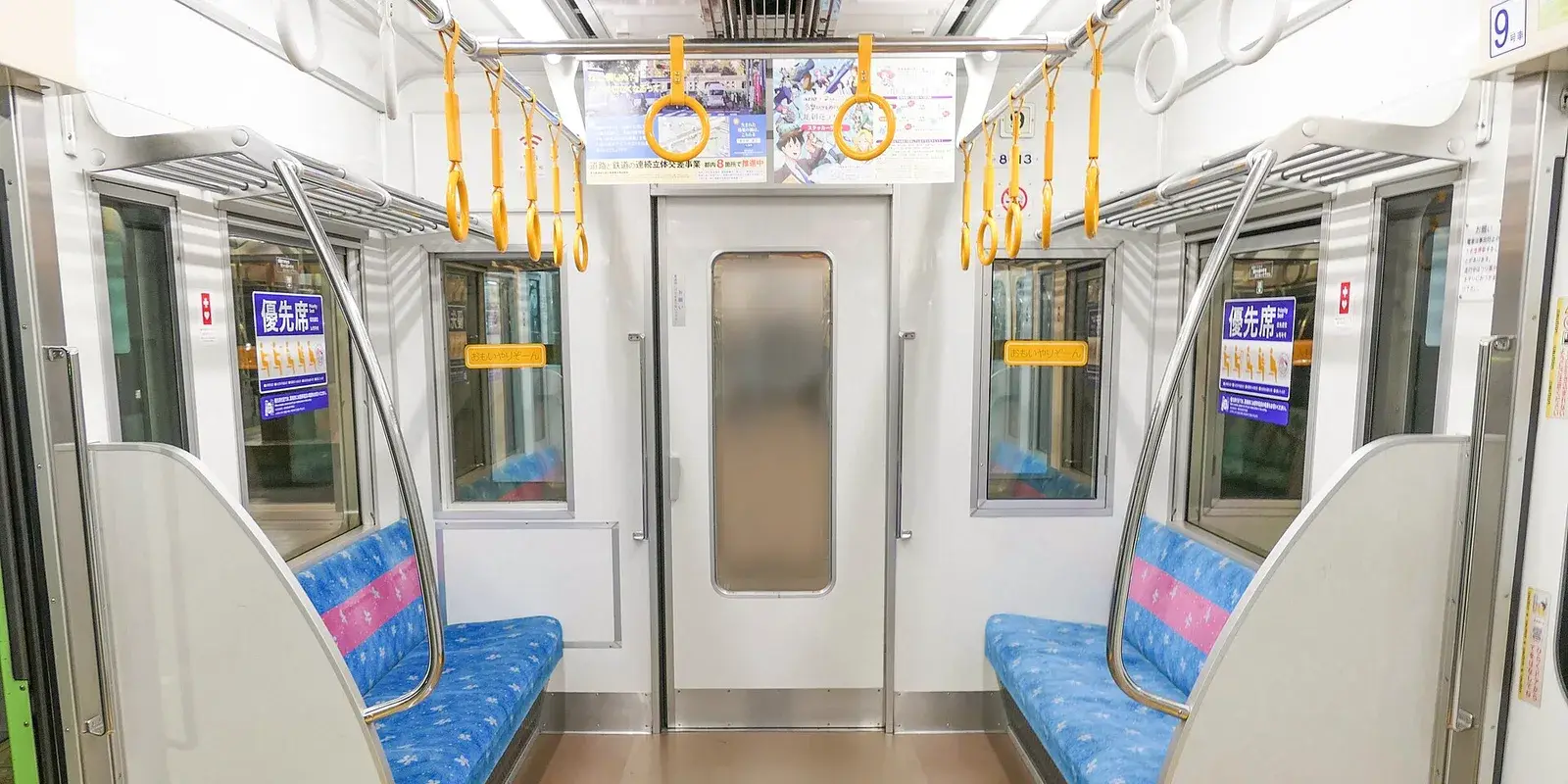 Interior of a Keio Line train in Japan showing empty blue priority seats with priority-seat signage and yellow straps, no passengers