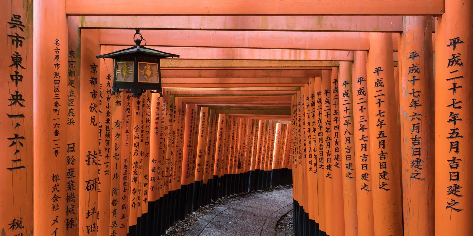 Vermilion torii gates lining a stone path with a hanging lantern at Fushimi Inari Taisha Shrine, Kyoto