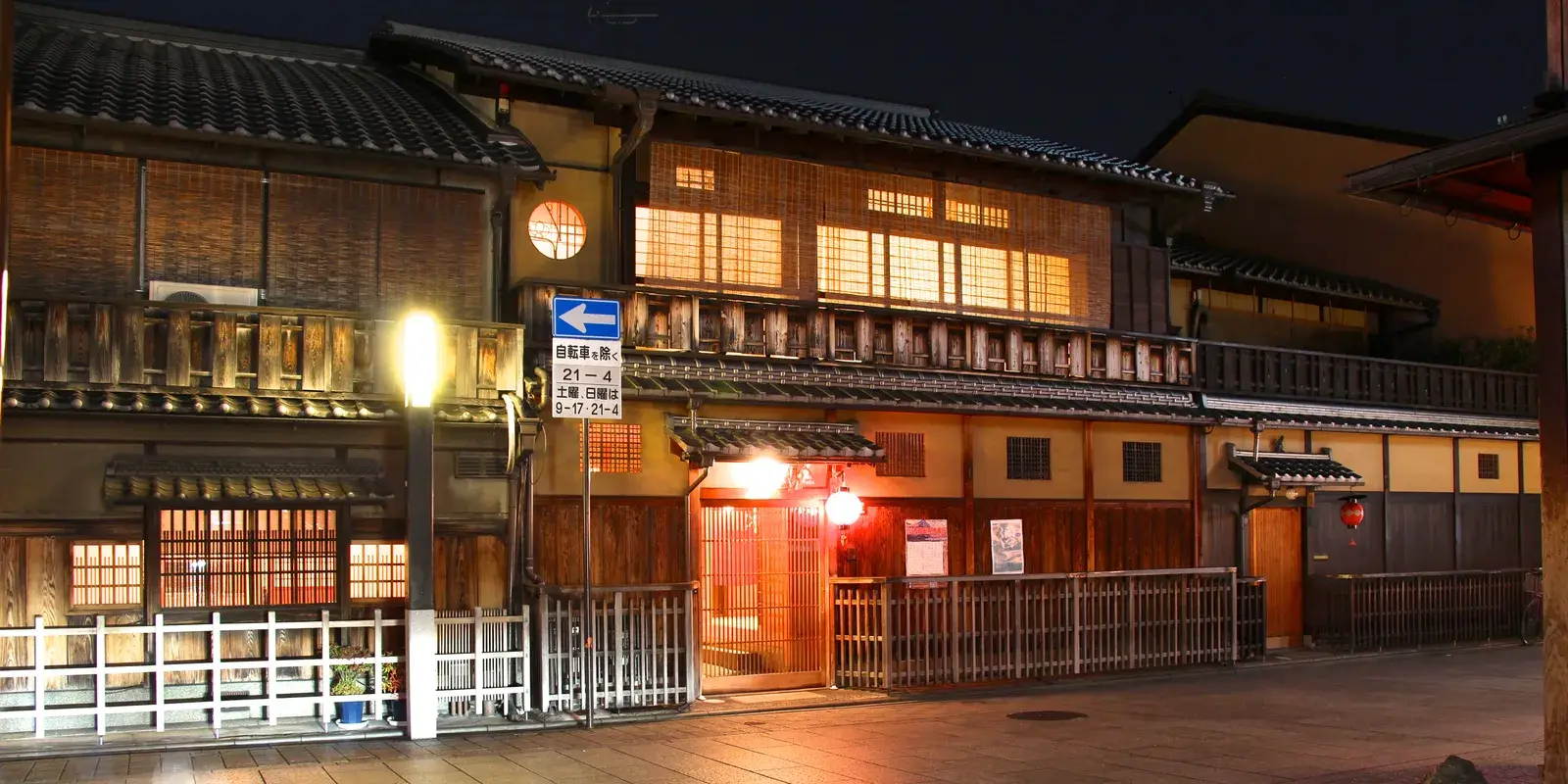 A quiet traditional wooden machiya street in the Gion district of Kyoto at night, lit by a glowing red lantern