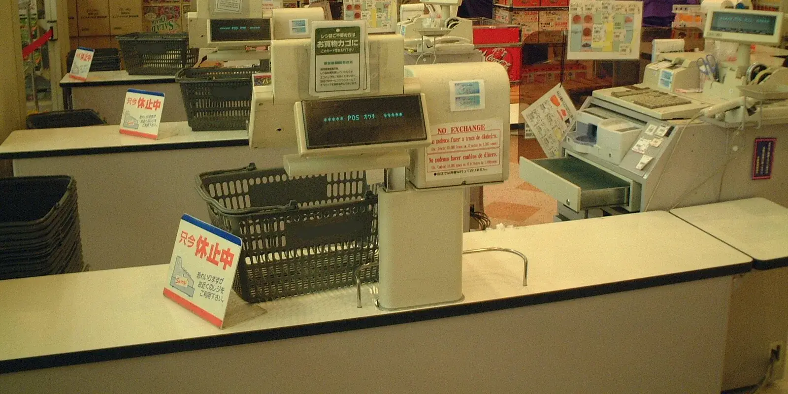 A Japanese supermarket checkout counter with a point-of-sale register, shopping baskets, and an open cash drawer holding money