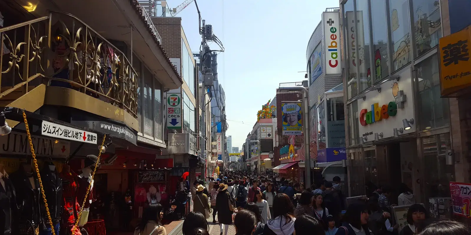 Crowds of people in everyday casual clothing walking down Takeshita Street, a busy shopping street in Harajuku, Tokyo