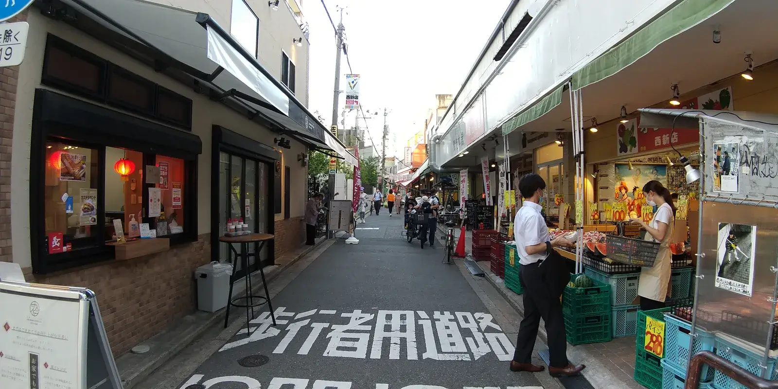 Shoppers at an open-air produce stall in the Nishijin covered shopping arcade in Fukuoka, with watermelons and price tags