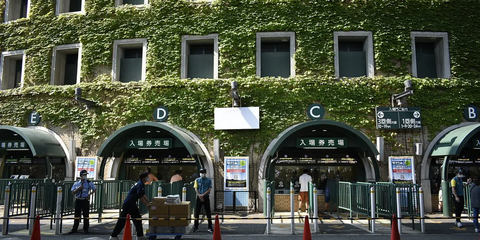 The ivy-covered facade of Hanshin Koshien Stadium with its arched ticket gates on a sunny summer day