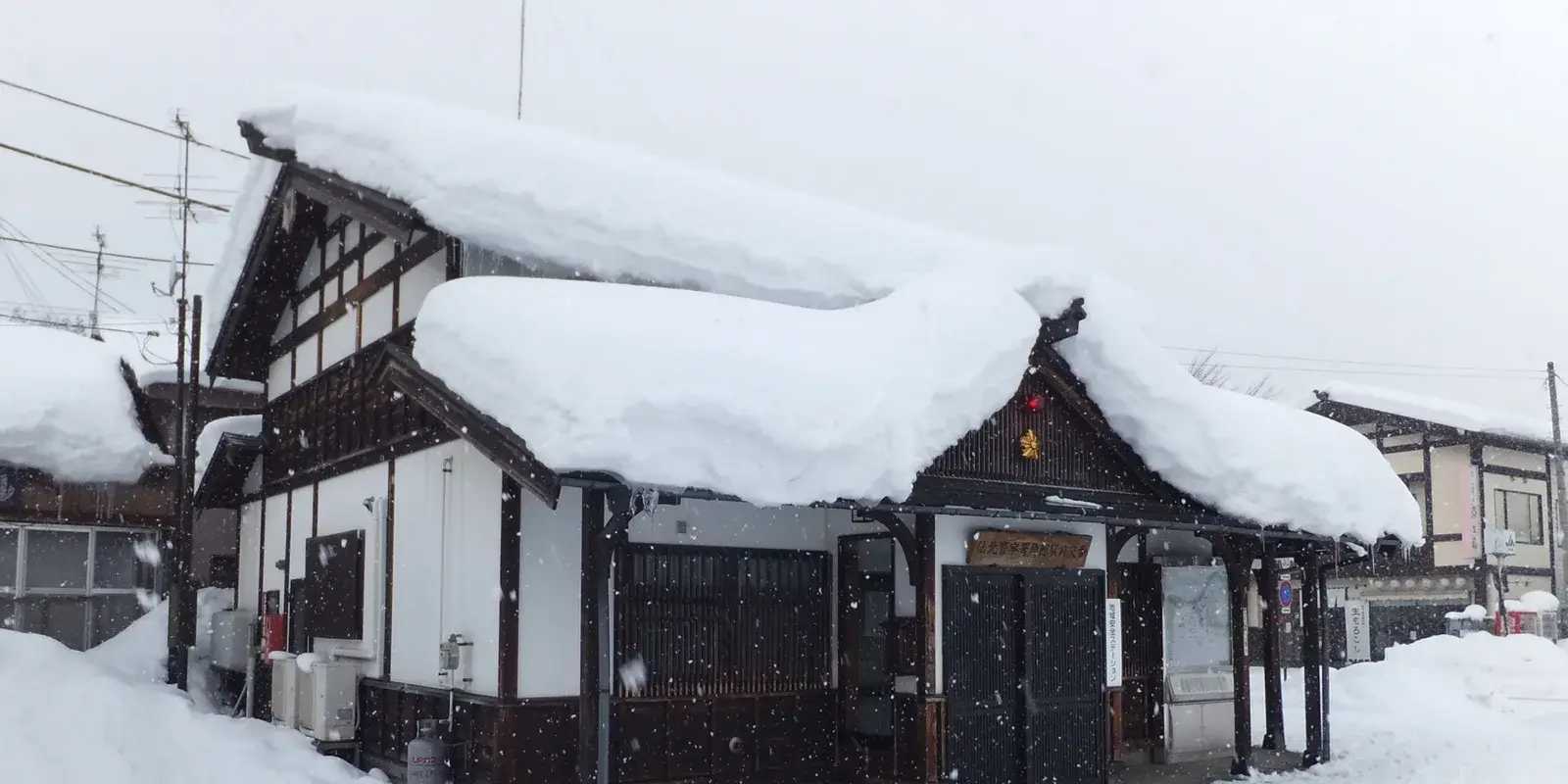 A traditional wooden Japanese koban (neighborhood police box) blanketed in deep snow in Kakunodate, Akita, with a red warning lantern and signboard at its entrance
