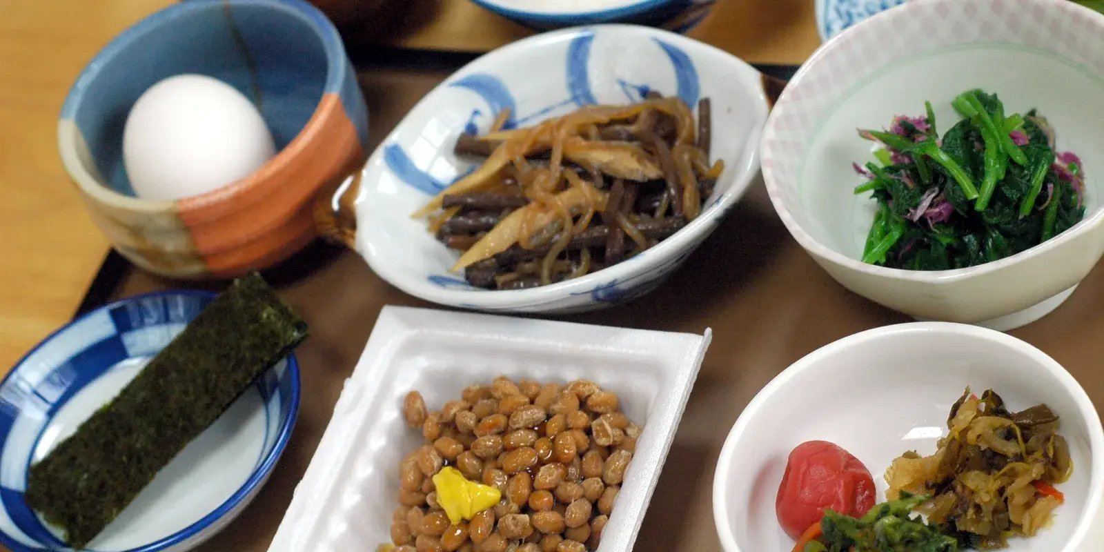 A traditional Japanese breakfast tray: miso soup, rice, grilled fish, simmered vegetables, spinach with sesame, natto, nori, umeboshi, and pickles