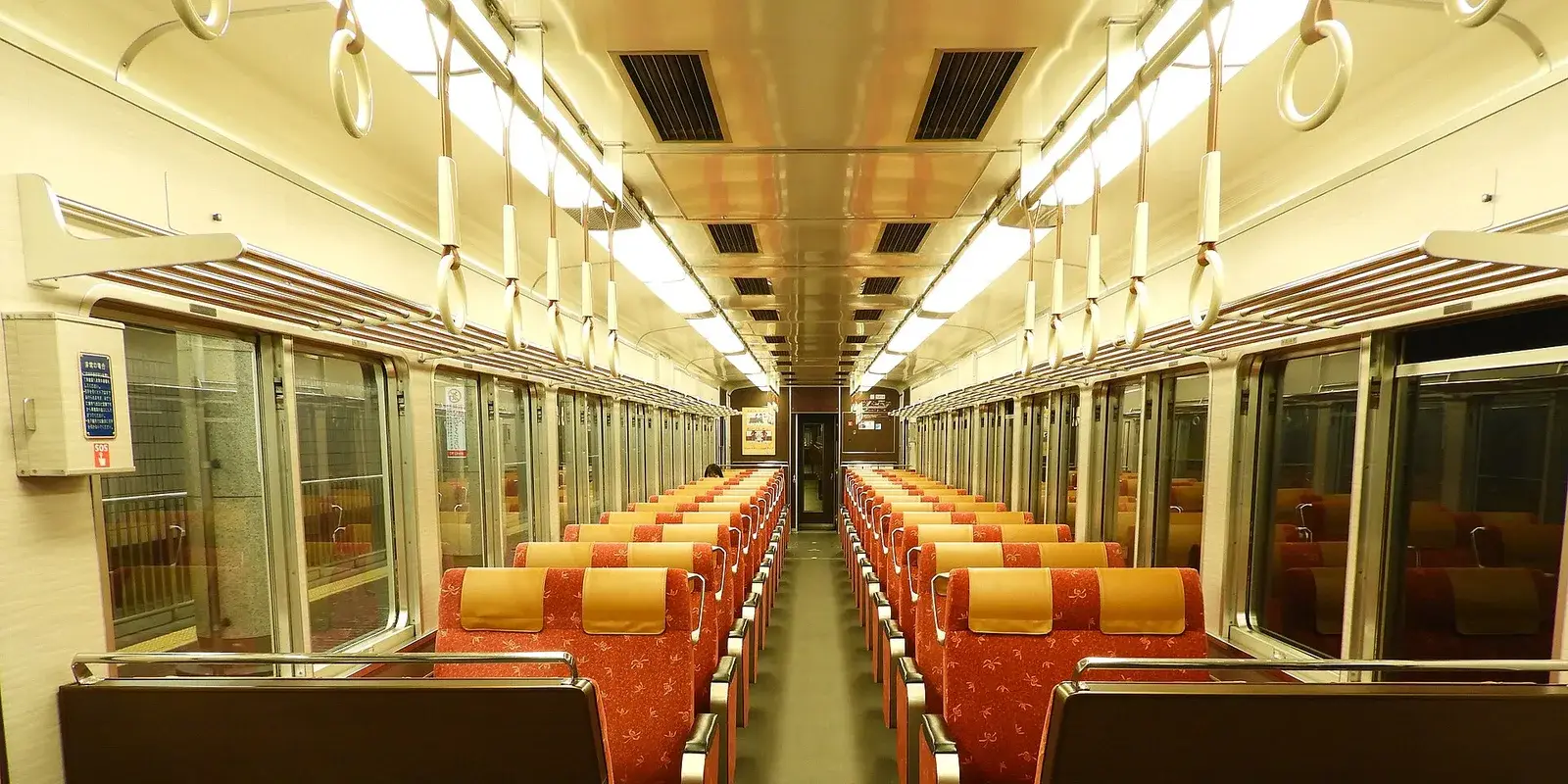 Quiet, empty Japanese train interior with rows of seats receding to a vanishing point under warm lighting