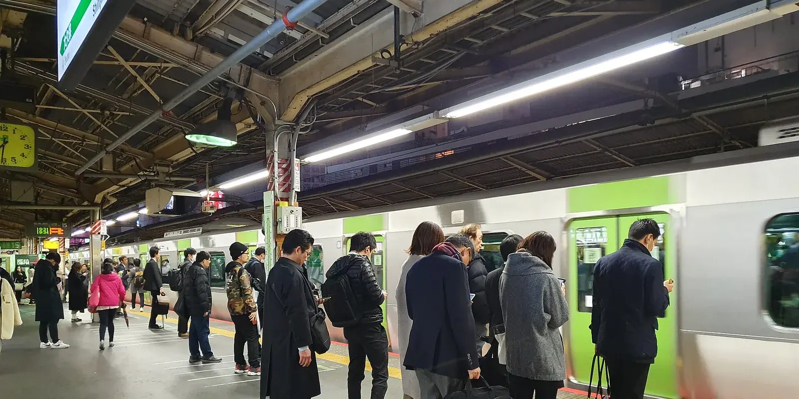Passengers waiting in orderly lines on a Yamanote Line platform at Shinjuku Station, Tokyo, as a train arrives