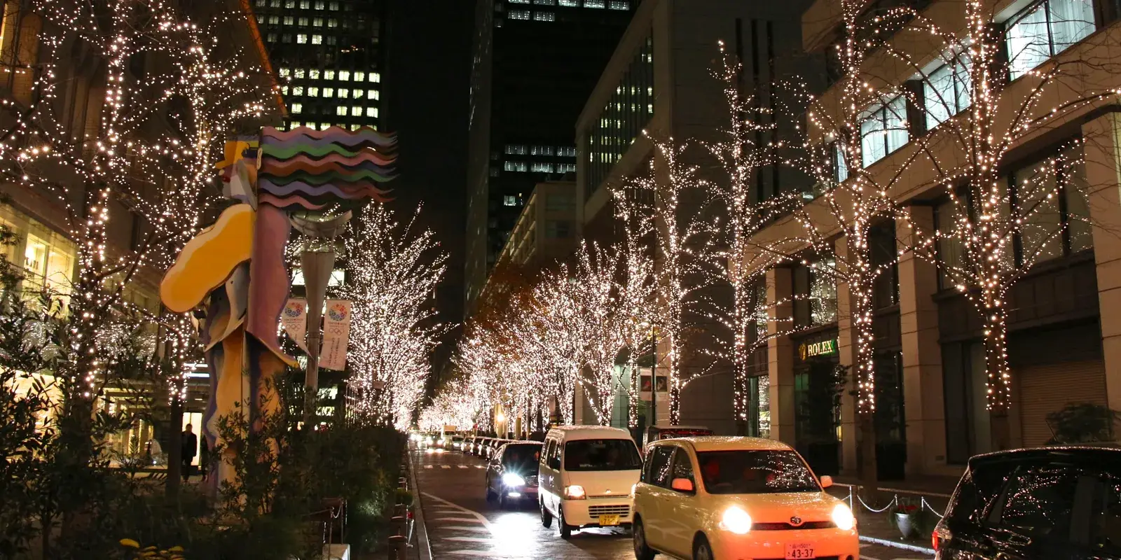Marunouchi Nakadori in Tokyo at night, its avenue of bare street trees wrapped end to end in warm champagne-gold lights