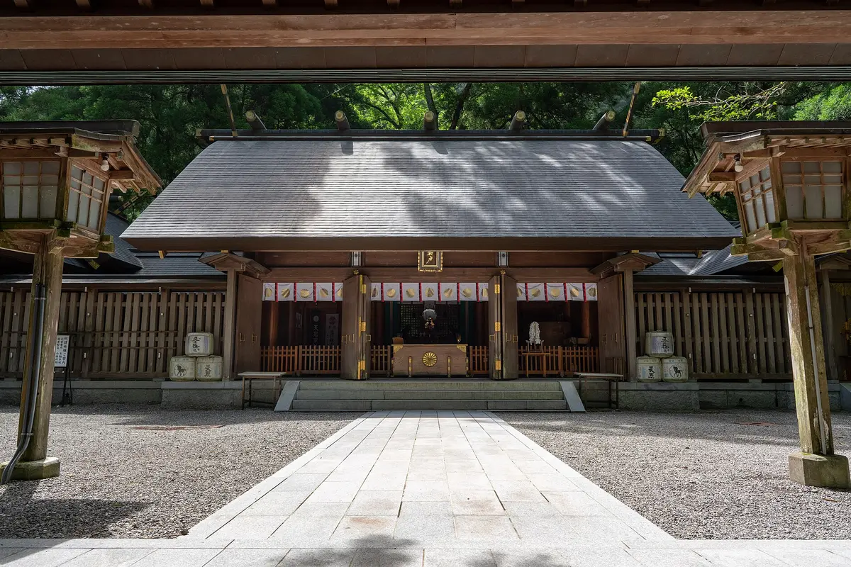 The wooden main hall of Amano-Iwato Shrine in Takachiho, seen down a stone path between two standing lanterns