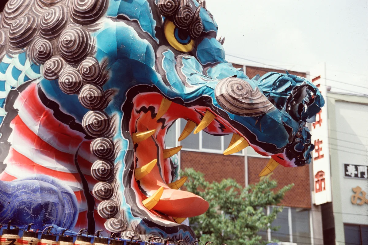 Close-up daytime view of a dragon-shaped Nebuta float showing its painted washi paper and wire-frame construction
