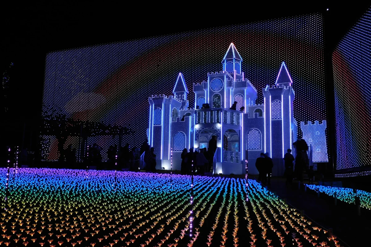 An illuminated castle structure and a field of colored lights at the Flower Fantasy winter light festival