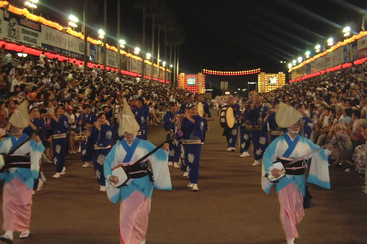 Awa Odori musicians walking with the dancers: shamisen players in front, flute players behind them, and a large taiko drum carried at the side