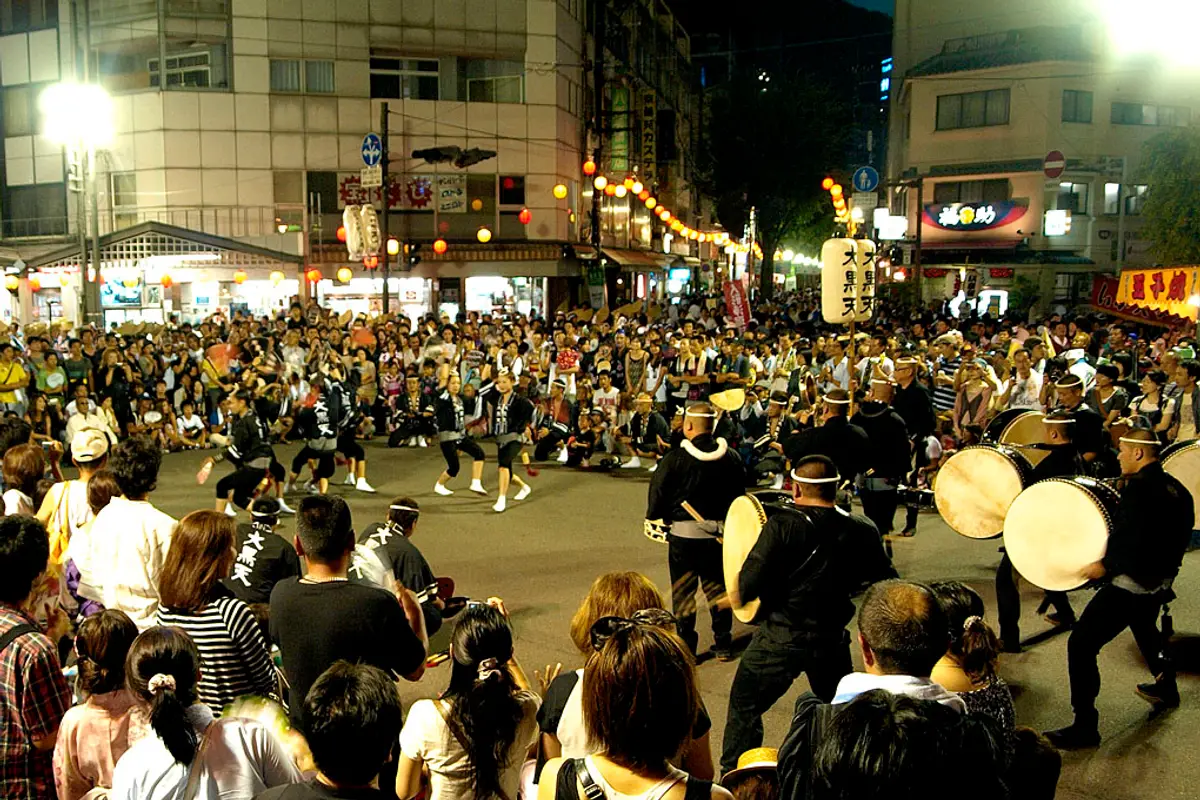 Dancers in the middle of an open street corner in Tokushima at night, ringed by onlookers, with large taiko drums to one side