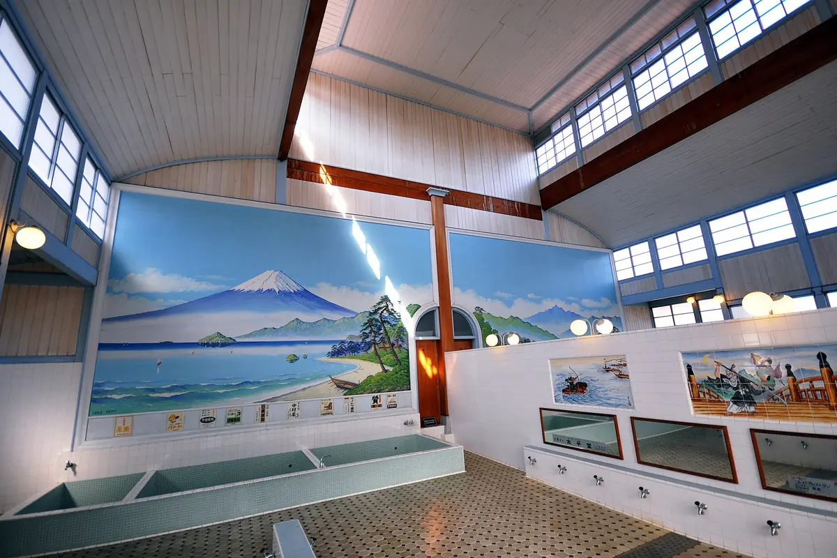 Empty tiled bathing hall of a prewar sento, with a painted Mount Fuji above the tubs and washing taps with mirrors along the side wall