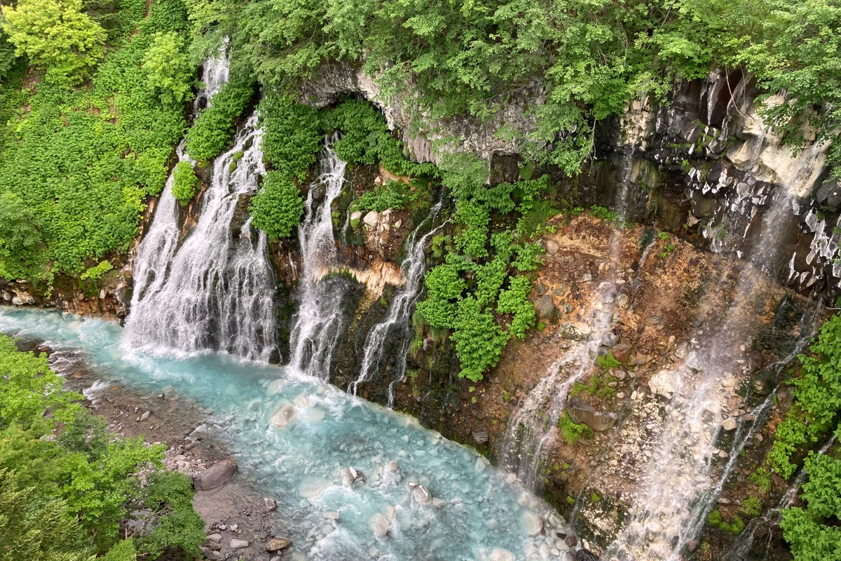 Nearby Shirahige Falls: threads of spring water spilling from a mossy cliff into the vivid blue Biei River