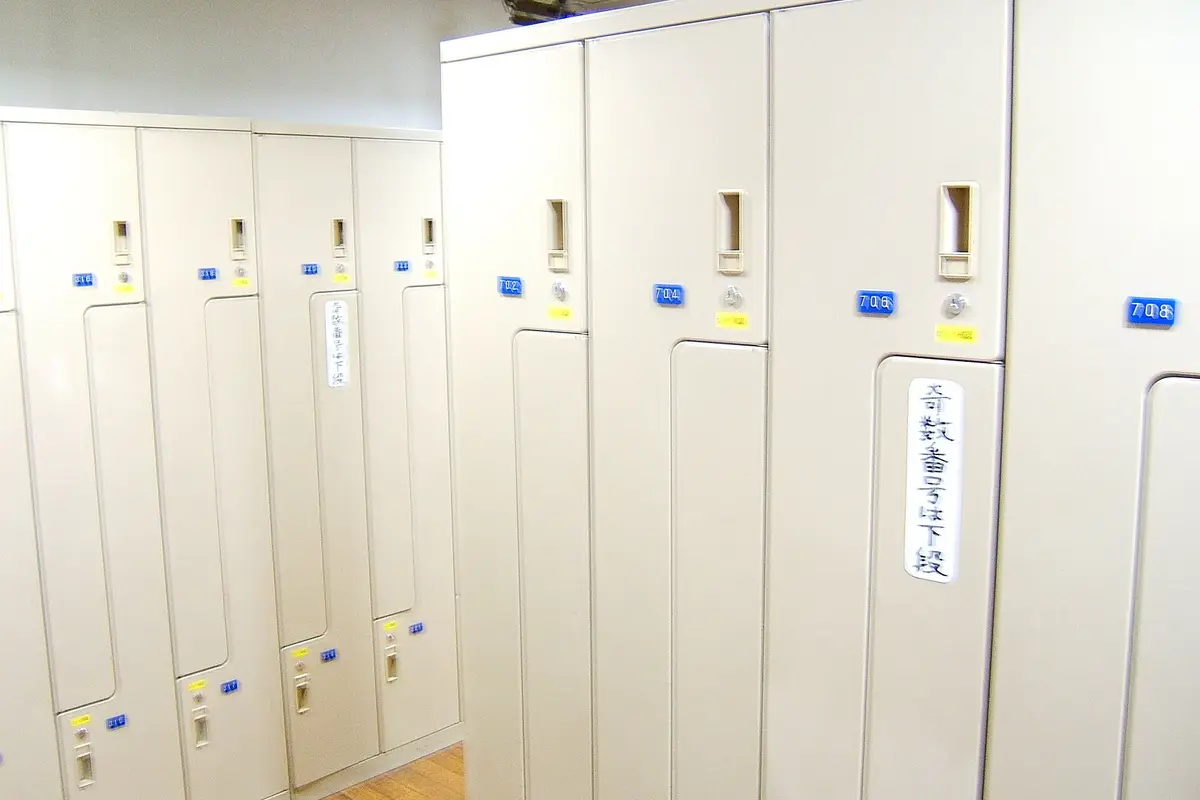 Rows of tall, narrow guest lockers with numbered plates and key locks in a capsule hotel