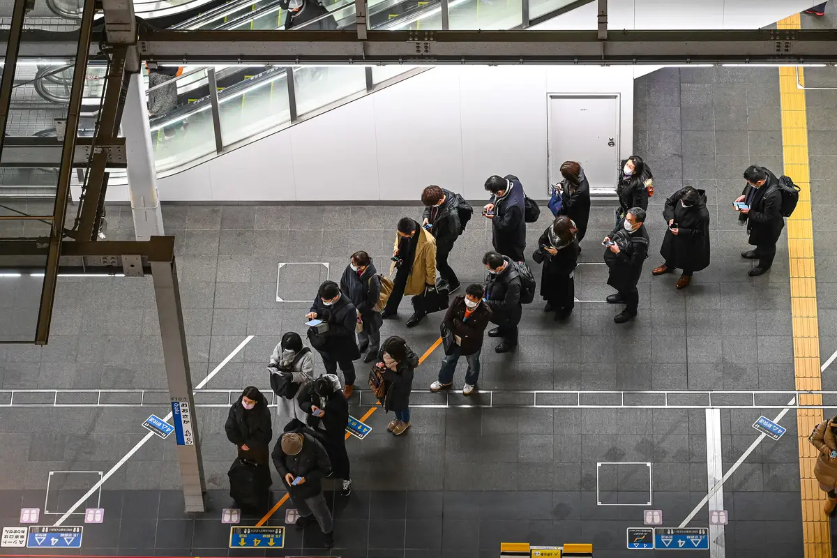 Commuters seen from above on an Osaka Station platform, standing in lines behind painted floor markings that show where each train door will open