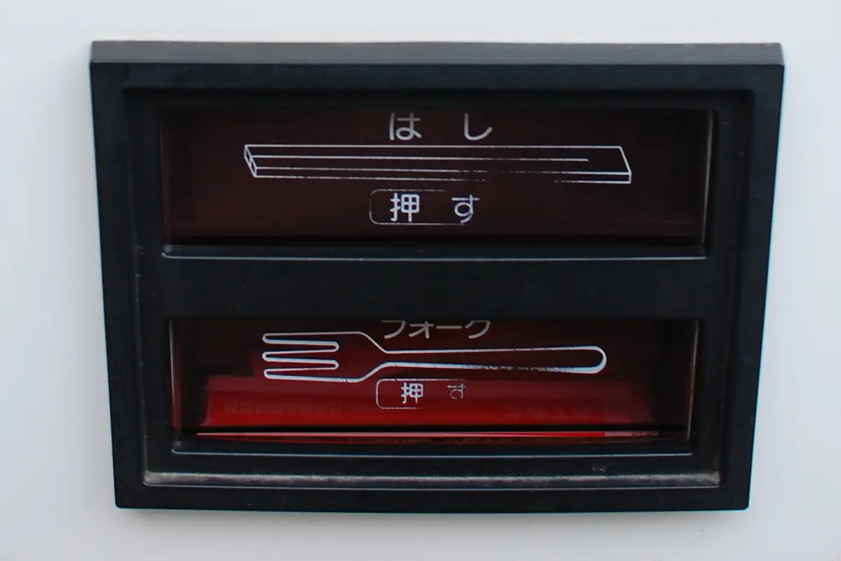 A utensil dispenser in Japan with two labelled slots, one for chopsticks and one for forks, each marked push